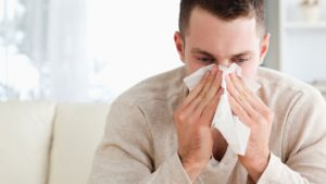 A man with seasonal allergic rhinitis blows his nose