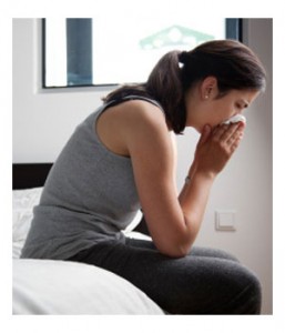 A woman with hay fever is blowing her nose on bed